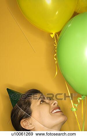 Stock Photo - Caucasian prime adult female wearing party hat with balloons.. Fotosearch
