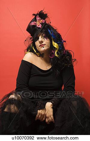Stock Image - Portrait of Caucasian woman in unique makeup and clothing against red background.. Fotosearch