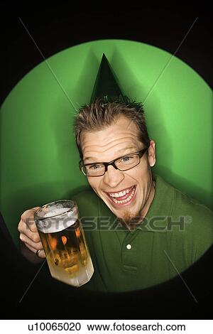 Stock Image - Vignette of adult Caucasian man on green background wearing green hat and holding beer.. Fotosearch