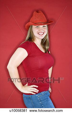 Stock Image - Young Caucasian female adult in red cowboy hat on red background.. Fotosearch