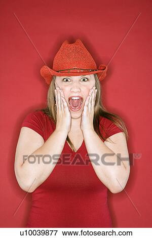 Young Caucasian female adult in red cowboy hat on red background with hands on face and mouth open. View Large Photo Image Stock Photo - Young Caucasian female adult in red cowboy hat on red background with hands on face and mouth open.. Fotosearch