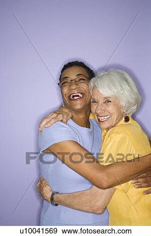 Stock Photo - Caucasian and African American mature adult female embracing.. Fotosearch