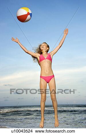 Picture - Caucasian pre-teen girl playing with beachball on beach.. Fotosearch