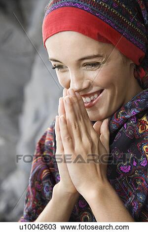 Stock Image - Caucasian young adult woman with hands together in prayer position holding up to face and smiling.. Fotosearch