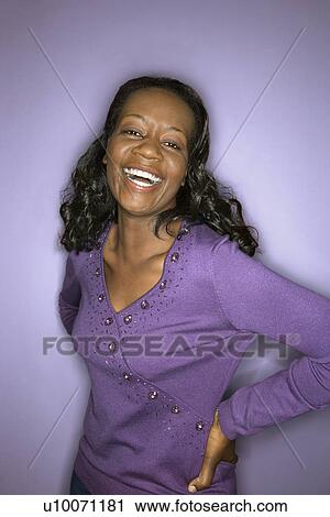 Stock Image - Portrait of laughing mid-adult African-American woman on purple background.. Fotosearch