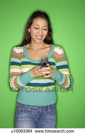 Portrait of smiling Multi-racial teen girl dialing cellphone standing in front of green background. View Large Photo Image Picture - Portrait of smiling Multi-racial teen girl dialing cellphone standing in front of green background.. Fotosearch