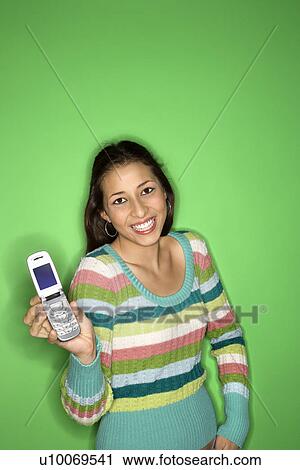 Stock Image - Portrait of smiling Multi-racial teen girl holding cellphone out standing in front of green background.. Fotosearch