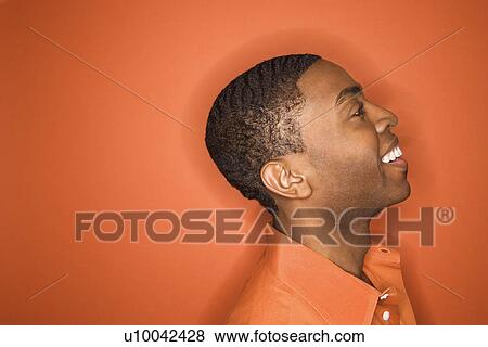 Stock Photo - Side view of smiling young African-American man on orange background.. Fotosearch