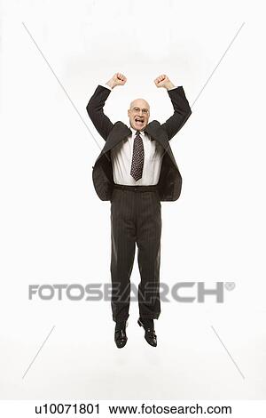 Stock Image - Smiling Caucasian middle-aged businessman jumping with arms raised.. Fotosearch