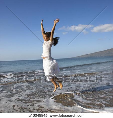 Stock Photography - Young Asian female jumping in air at the shoreline.. Fotosearch
