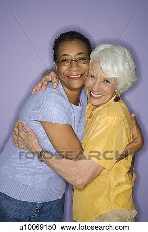 Stock Image - Caucasian and African American mature adult female embracing.. Fotosearch