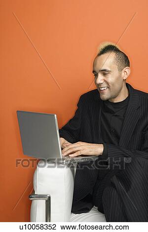 Caucasian man in suit with mohawk smiling typing on laptop against orange background. View Large Photo Image Stock Image - Caucasian man in suit with mohawk smiling typing on laptop against orange background.. Fotosearch