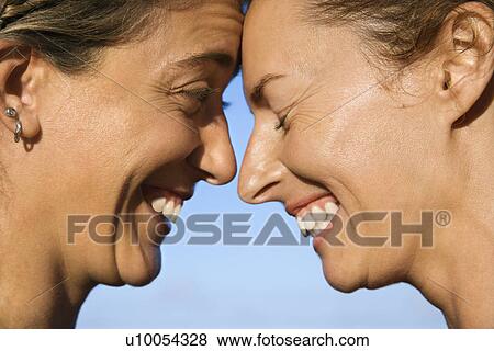 Stock Photo - Caucasian mid-adult women with their heads together smiling.. Fotosearch