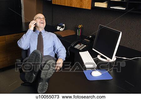 Caucasian middle-aged businessman in office sitting with feet on desk talking and laughing on cellphone. View Large Photo Image Stock Image - Caucasian middle-aged businessman in office sitting with feet on desk talking and laughing on cellphone.. Fotosearch