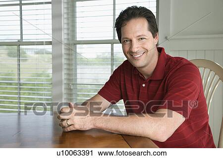 Stock Image - Caucasian prime adult male portrait sitting at table. Portrait of Caucasian mid-adult woman sitting at table, looking at viewer, smiling.. Fotosearch