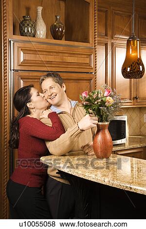 Caucasian woman kissing Caucasian man on cheek as he arranges flowers in vase in kitchen. View Large Photo Image Stock Photo - Caucasian woman kissing Caucasian man on cheek as he arranges flowers in vase in kitchen.. Fotosearch