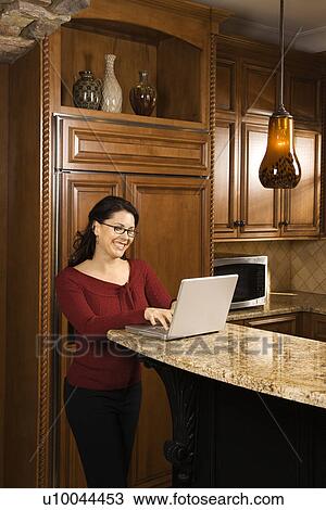 Caucasian woman standing at kitchen counter typing on laptop computer and smiling. View Large Photo Image Stock Image - Caucasian woman standing at kitchen counter typing on laptop computer and smiling.. Fotosearch