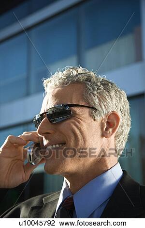 Stock Image - Close up side view of prime adult Caucasian man in suit talking on cellphone in urban setting.. Fotosearch