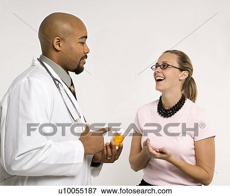Stock Photo - Mid-adult African-American doctor and Caucasion mid-adult female patient discussing medication.. Fotosearch