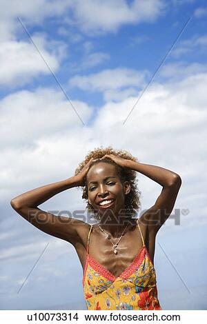 Picture - Mid-adult Black female with hands on forehead with clouds in background.. Fotosearch