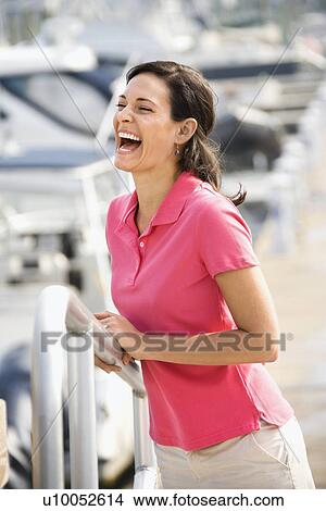 Picture - Portrait of Caucasian mid-adult female holding railing and laughing at harbor. . Fotosearch