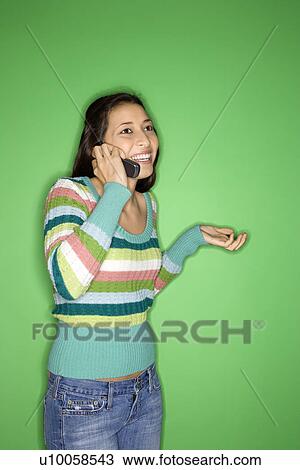 Stock Image - Portrait of Multi-racial teen girl talking on cellphone and smiling standing against green background.. Fotosearch