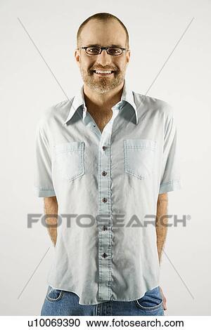 Stock Image - Portrait of smiling Caucasian man wearing eyeglasses standing against white background.. Fotosearch