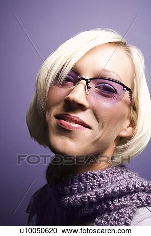 Stock Image - Portrait of smiling young adult Caucasian blond woman on purple background wearing sunglasses and scarf.. Fotosearch