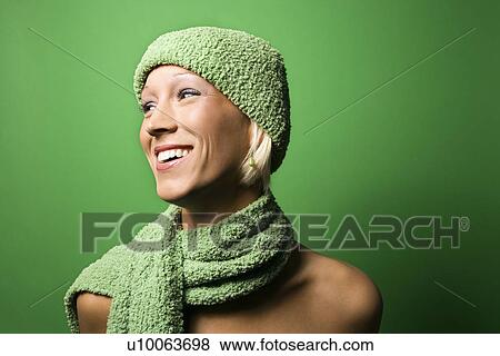 Stock Photo - Portrait of smiling young adult Caucasian woman on green background wearing winter hat and scarf.. Fotosearch