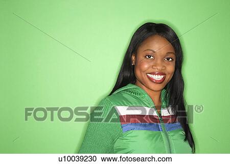 Stock Image - Smiling African-American mid-adult woman in green coat on green background.. Fotosearch