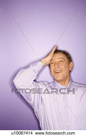 Smiling middle-aged Caucasian man on purple background with his hand on his forehead. View Large Photo Image Picture - Smiling middle-aged Caucasian man on purple background with his hand on his forehead.. Fotosearch