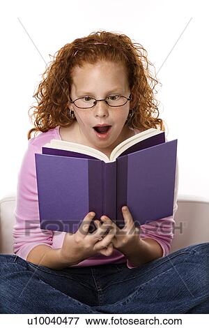 Stock Photo - Caucasian female child sitting reading book looking surprised.. Fotosearch