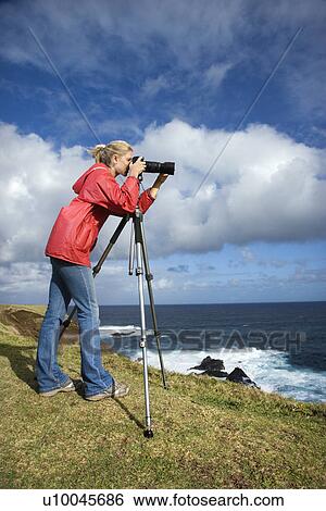 Caucasian mid-adult woman looking through camera on tripod on cliff overlooking ocean in Maui, Hawaii. View Large Photo Image Stock Photograph - Caucasian mid-adult woman looking through camera on tripod on cliff overlooking ocean in Maui, Hawaii.. Fotosearch