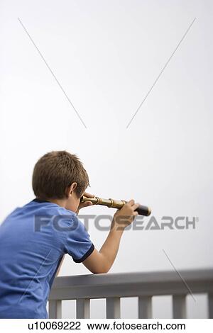 Stock Image - Caucasian pre-teen boy leaning on railing looking through telescope.. Fotosearch