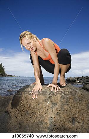 Stock Image - Caucasian young adult woman squatting on large rock.. Fotosearch
