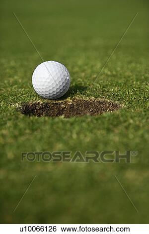 Stock Photograph - Close up image of golf ball close to the hole.. Fotosearch
