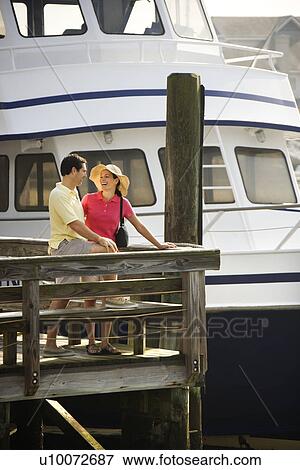 Mid-adult Caucasian couple at dock looking at each other with boat in background. View Large Photo Image Stock Photo - Mid-adult Caucasian couple at dock looking at each other with boat in background.. Fotosearch