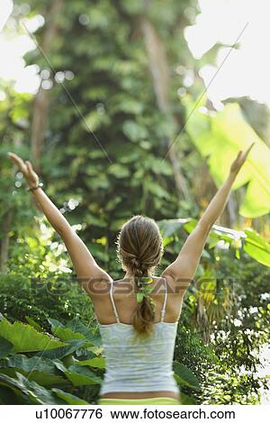 Stock Photograph - Rear view of Caucasian mid-adult woman holding arms out in yoga position.. Fotosearch
