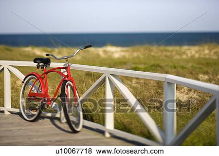 Stock Photo - Red beach cruiser bicycle leaning against walkway rail on beach on Bald Head Island, North Carolina.. Fotosearch
