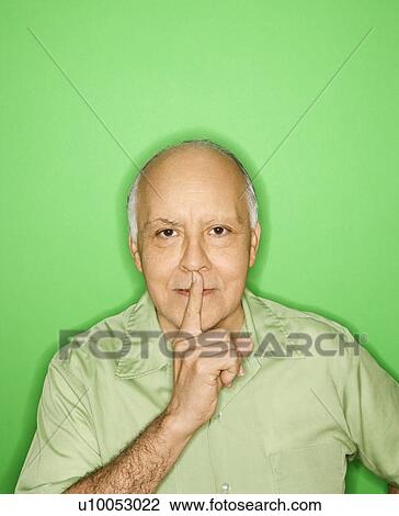 Stock Image - Caucasian mature adult male holding finger to mouth.. Fotosearch