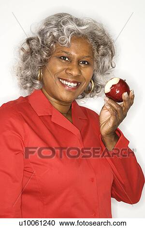 Stock Image - Mature adult African American female holding half eaten apple smiling.. Fotosearch