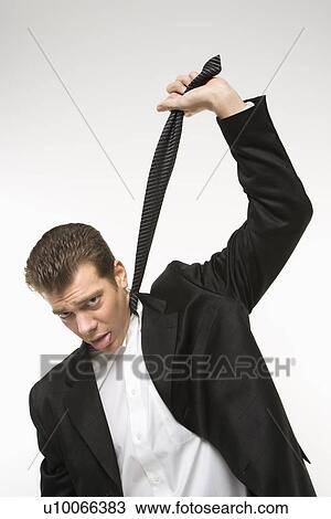 Stock Image - Caucasian mid-adult man pulling necktie out to choke himself while making facial expression.. Fotosearch