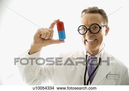 Picture - Mid-adult Caucasian male doctor wearing eyeglasses holding an oversized medical pill.. Fotosearch