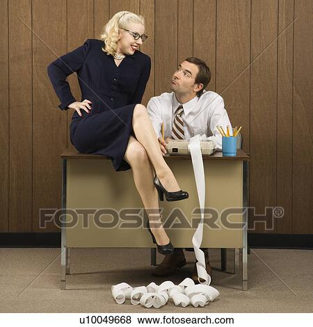 Mid-adult Caucasian male sitting at desk looking at Caucasian female sitting on desk. View Large Photo Image Stock Photo - Mid-adult Caucasian male sitting at desk looking at Caucasian female sitting on desk.. Fotosearch