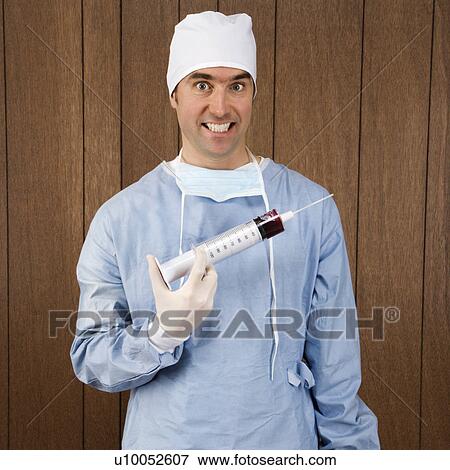 Stock Photo - Mid-adult Caucasian male surgeon holding oversized syringe and smiling maniacally.. Fotosearch