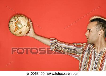 Profile of Caucasian man with mohawk holding globe against red background. View Large Photo Image Stock Photo - Profile of Caucasian man with mohawk holding globe against red background.. Fotosearch