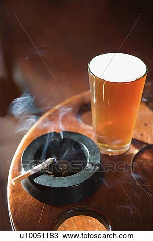 Stock Image - Full beer glass and cigarette with smoke rising in nightclub.. Fotosearch