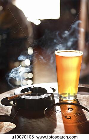 Full beer glass and cigarette with smoke rising in nightclub. View Large Photo Image Stock Photography - Full beer glass and cigarette with smoke rising in nightclub.. Fotosearch