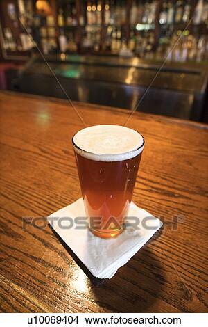 Picture - Glass of beer with napkin on bar.. Fotosearch
