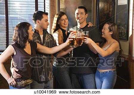 Stock Photo - Group of young friends hanging out in pub and toasting with their beers.. Fotosearch